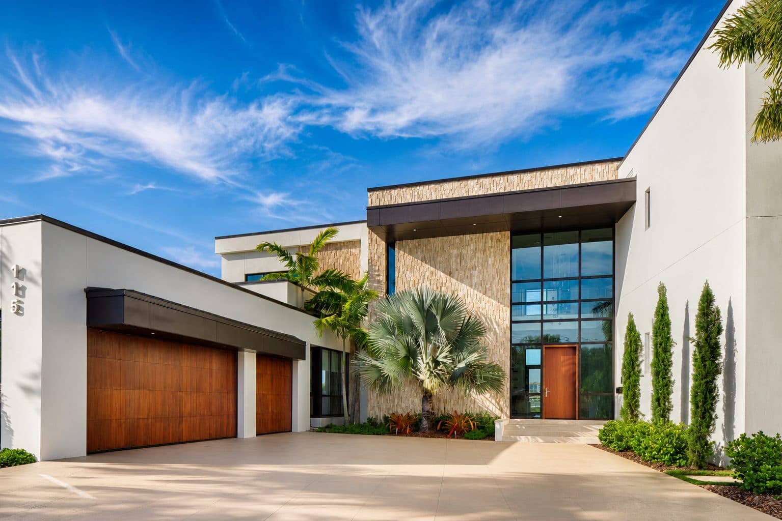 Craft House front entry with split-face stone feature wall, two-story glazing, and walnut garage doors